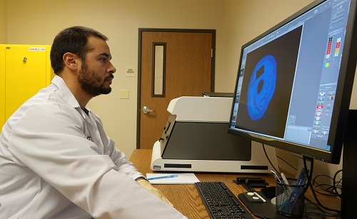 Man in lab coat examining image on computer monitor.